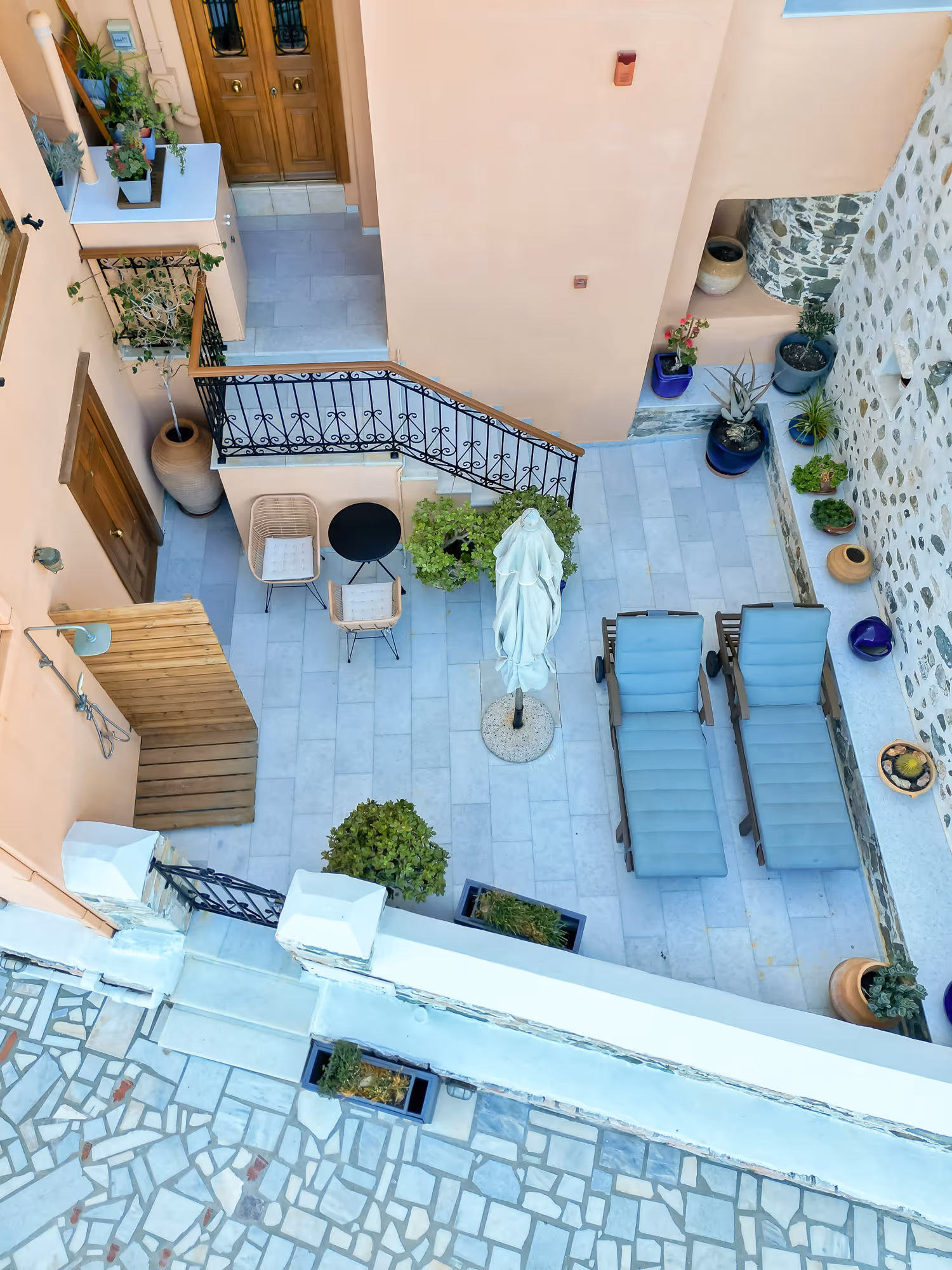 Top-down view of a courtyard with two blue lounge chairs, potted plants, table, and chairs.