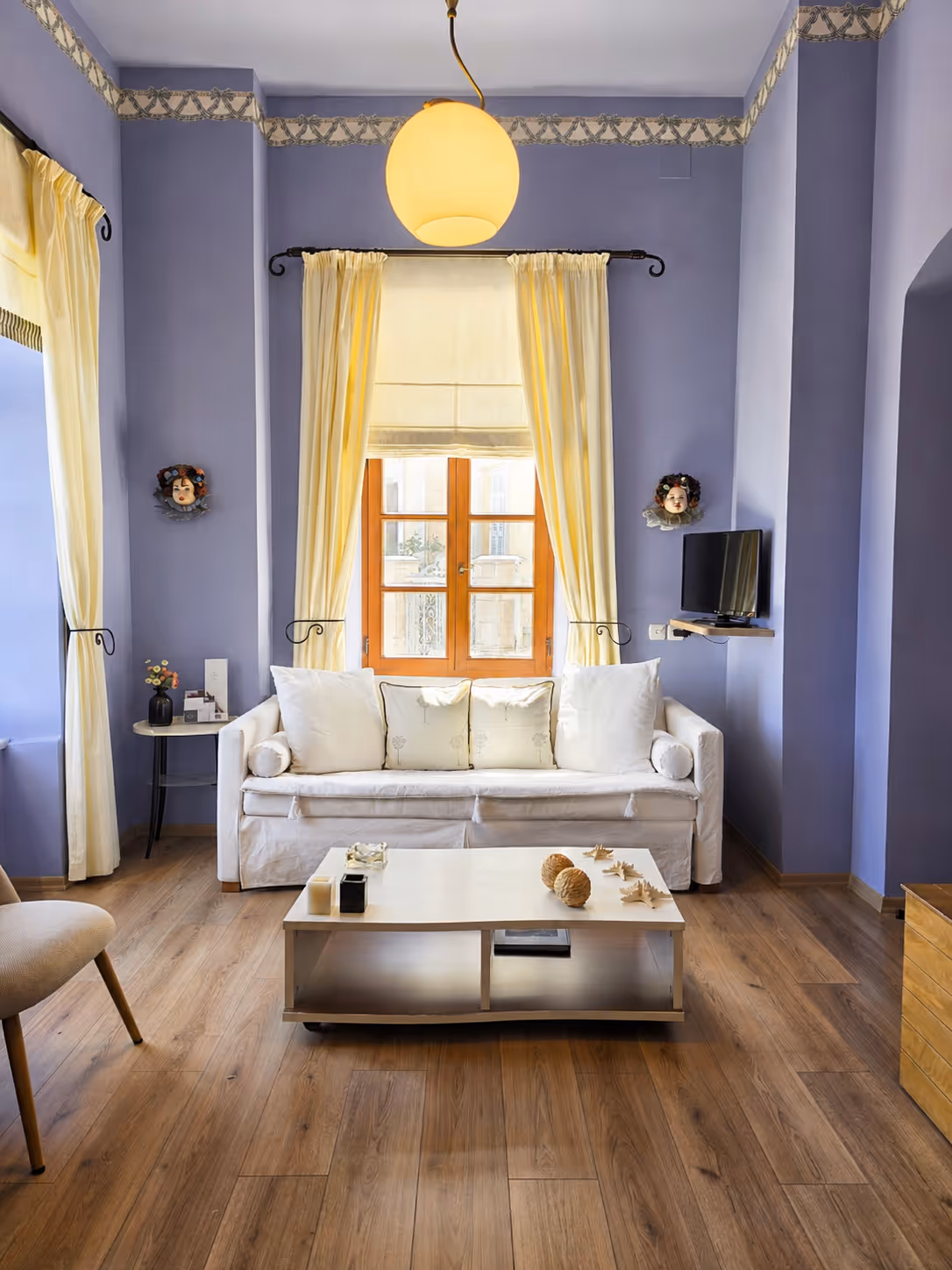 Cozy living room with a white sofa, wooden floor, blue walls, yellow curtains, and a round ceiling light.