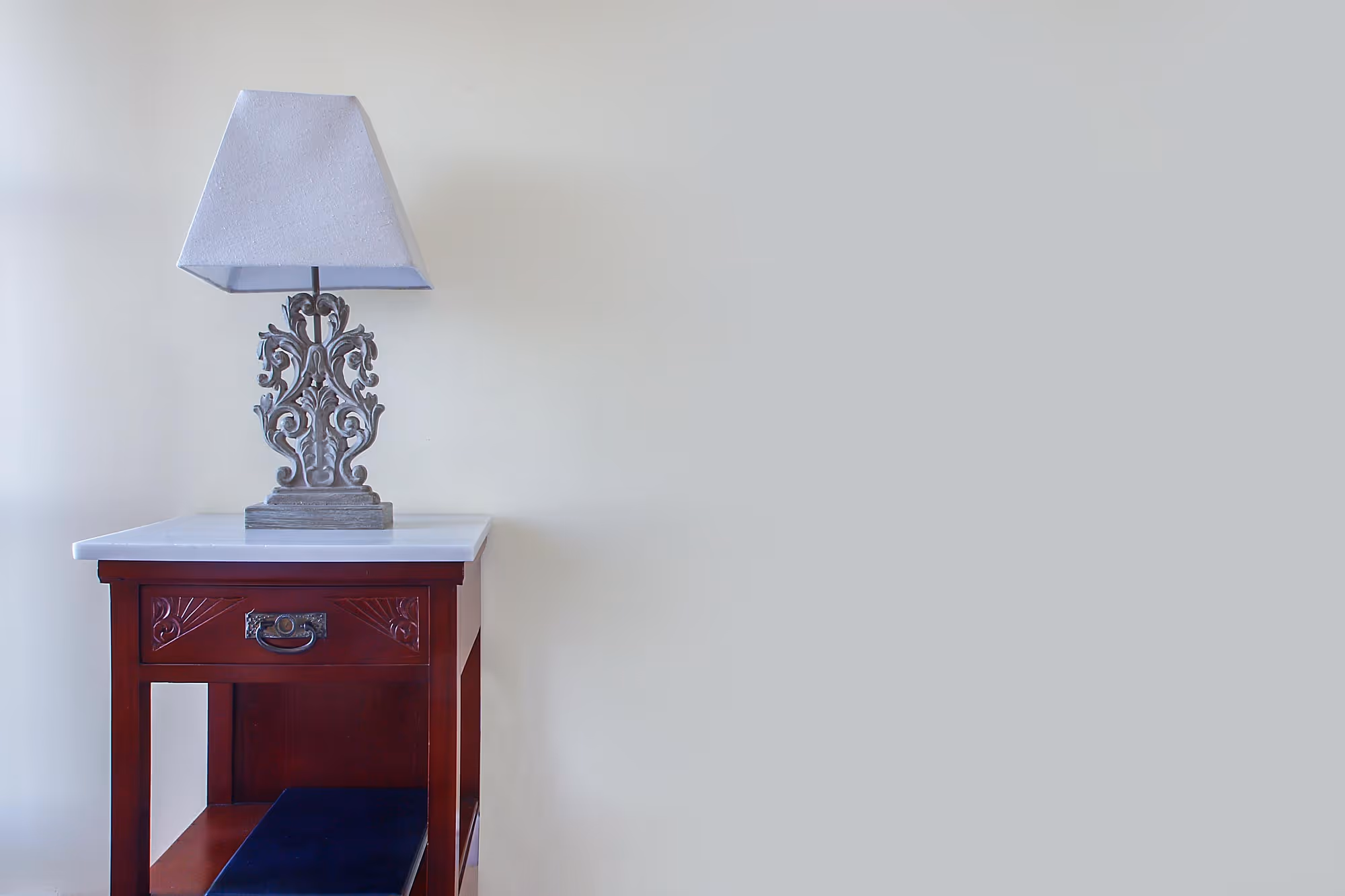 Decorative table lamp with white shade on a wooden nightstand against a plain light wall.