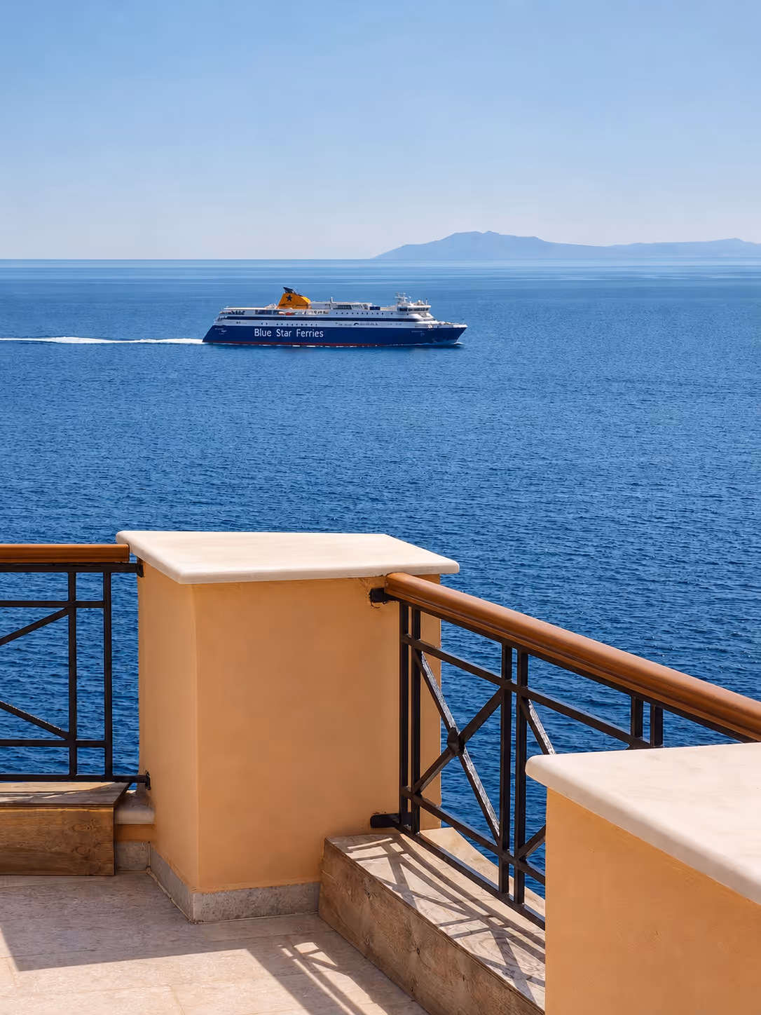 Blue Star Ferries ship sailing on calm blue sea with a terrace railing in foreground.