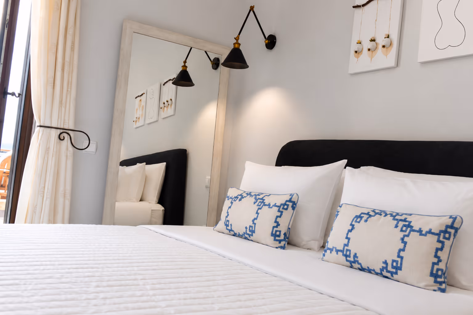 Modern bedroom with white bedding, blue patterned pillows, a black headboard, and a large mirror.