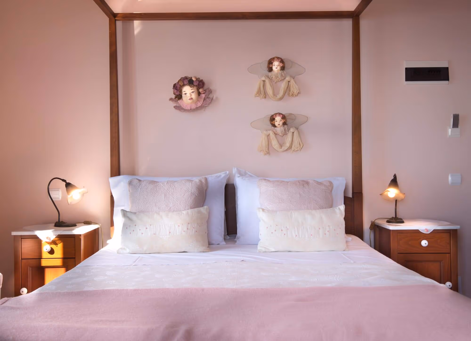 Pink-themed bedroom with a double bed featuring wooden canopy frame, two sets of pillows, and angel-themed wall decor above.